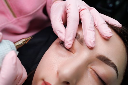 The master fingers the upper eyelid of the eye to apply permanent makeup. Permanent eye makeup